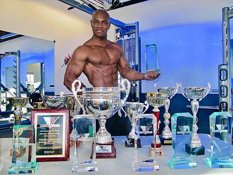 Antony Bessala derriere une table de trophees dont une plaque Musclemania de Las Vegas